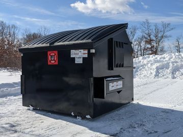 A black dumpster on a snowy ground with clear blue sky.