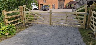 Wooden gate at driveway entrance with parked cars.