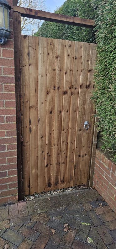Wooden garden gate between brick walls and hedges.