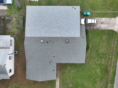 Aerial view of a house with a gray roof and a white car parked on the driveway.