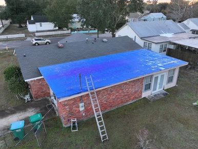 House with a blue tarp covering part of the roof and a ladder leaning against the wall.