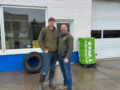 Two men stand outside a tire shop on a wet day.
