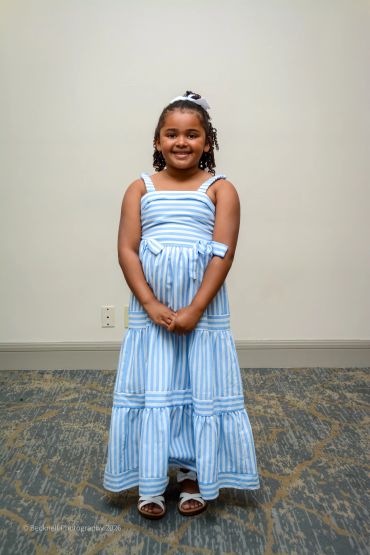 A young girl in a blue and white striped dress smiling at the camera.