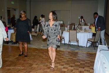 Women dancing at an indoor event with tables and chairs in the background.