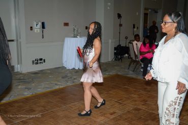 Two women dancing at an indoor event on a wooden dance floor.