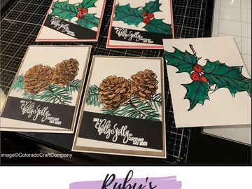 Handmade holiday cards featuring pinecones and holly designs on a crafting mat.