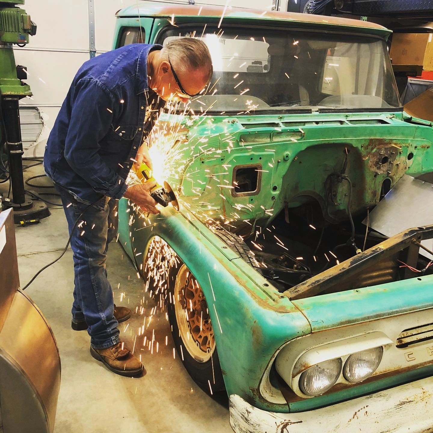 Man grinding a rusty old truck in a garage.