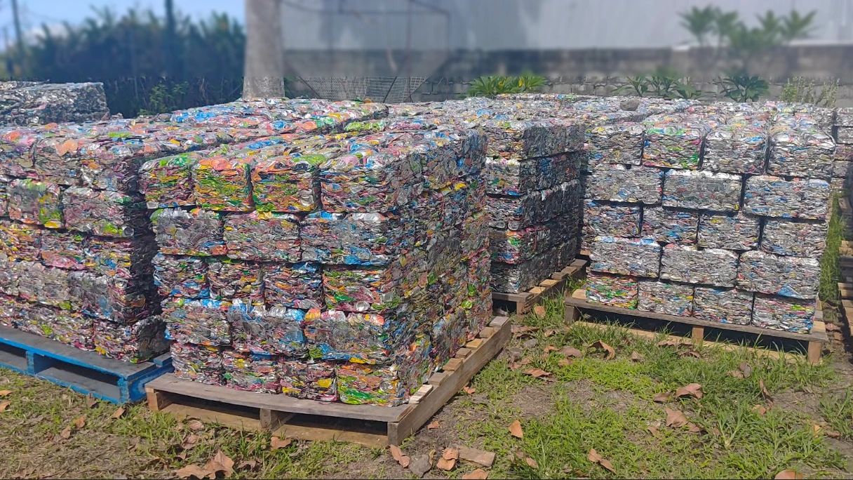 Stacks of compressed recyclable plastic waste on pallets outdoors.