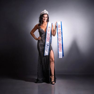 Woman in a crown and gown holding a sash.