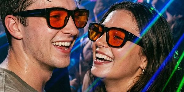 Two people smiling and wearing orange glasses with colorful lights around.