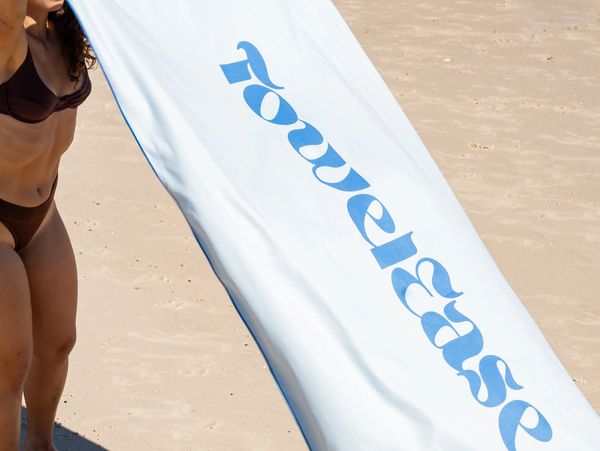 White and blue beach towel getting placed on the beach