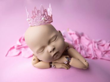 Sleeping baby doll wearing a pink crown on a pink background.