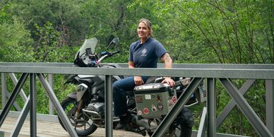 Joy Beth Cottle on a dual sport adventure bike on the bridge over her creek