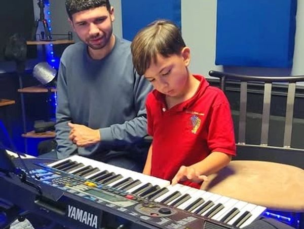 A man teaches a young boy to play a Yamaha keyboard.