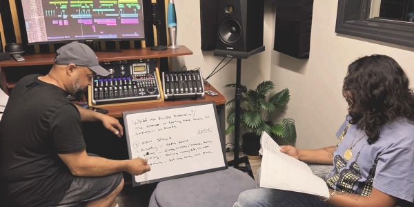 Two men collaborate in a music studio with a whiteboard and mixing equipment.
