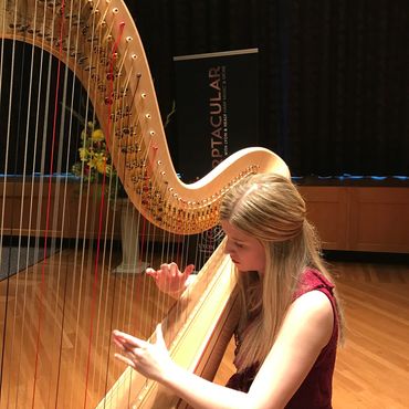 A woman playing a harp on a stage with a sign in the background.