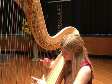 A woman playing a harp on a stage with a sign in the background.