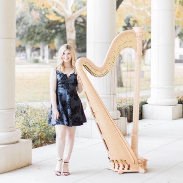 Woman in a black dress standing beside a harp outdoors.