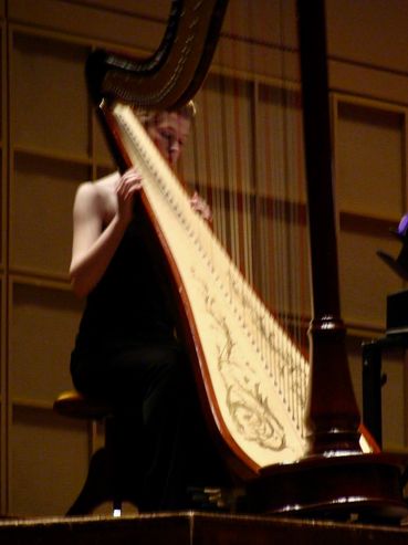 Musician playing a large harp on stage in a concert hall.