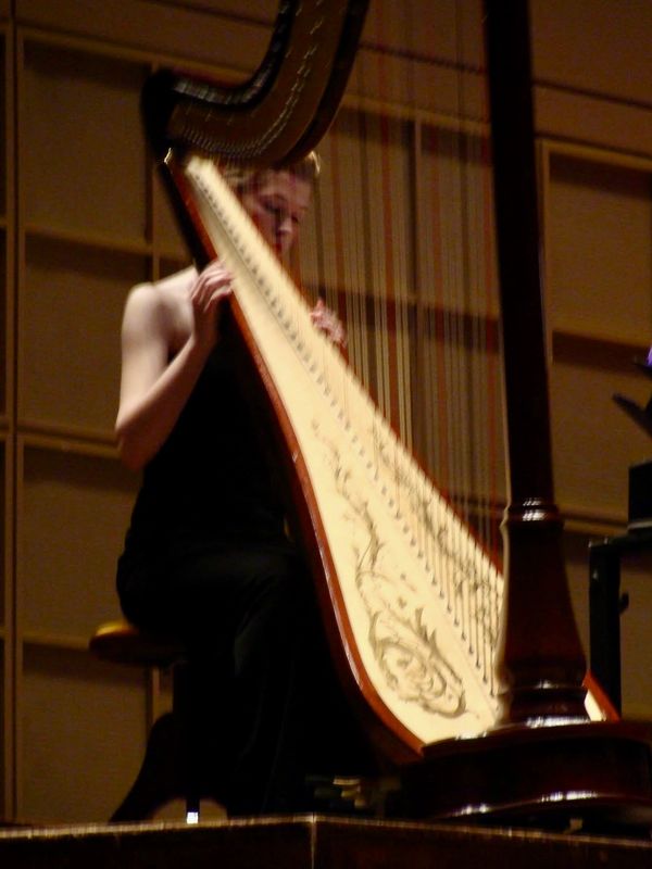 A musician playing a large harp on stage.