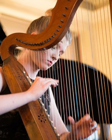 Young woman playing a harp with focused expression.