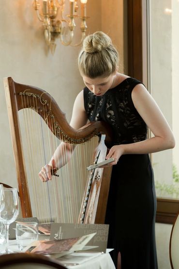 A woman in a black dress tuning a wooden harp.