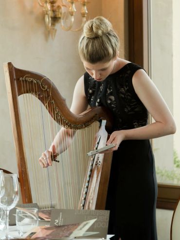 A woman in a black dress tuning a wooden harp.