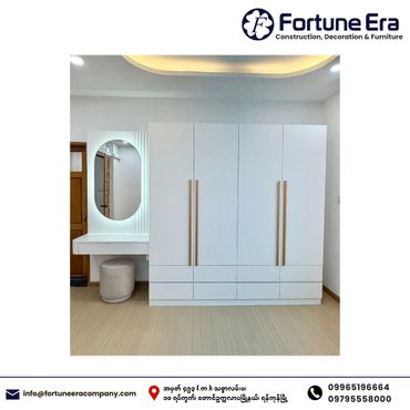 Modern white wardrobe with large handles and a vanity area with a round mirror.