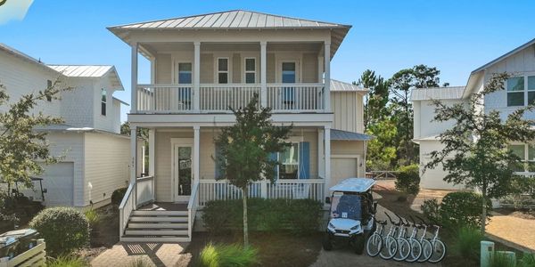Two-story house with front porch, golf cart, and bicycles on a sunny day.