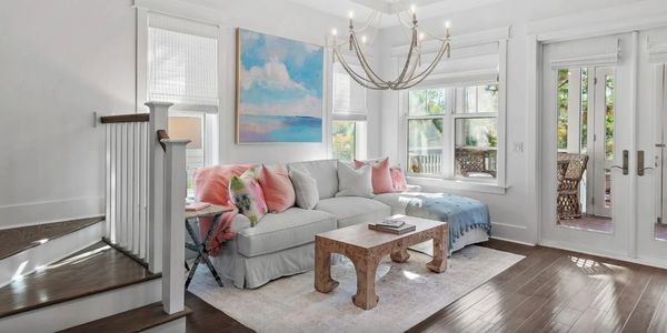 Bright living room with pastel pillows, wooden coffee table, and large windows.