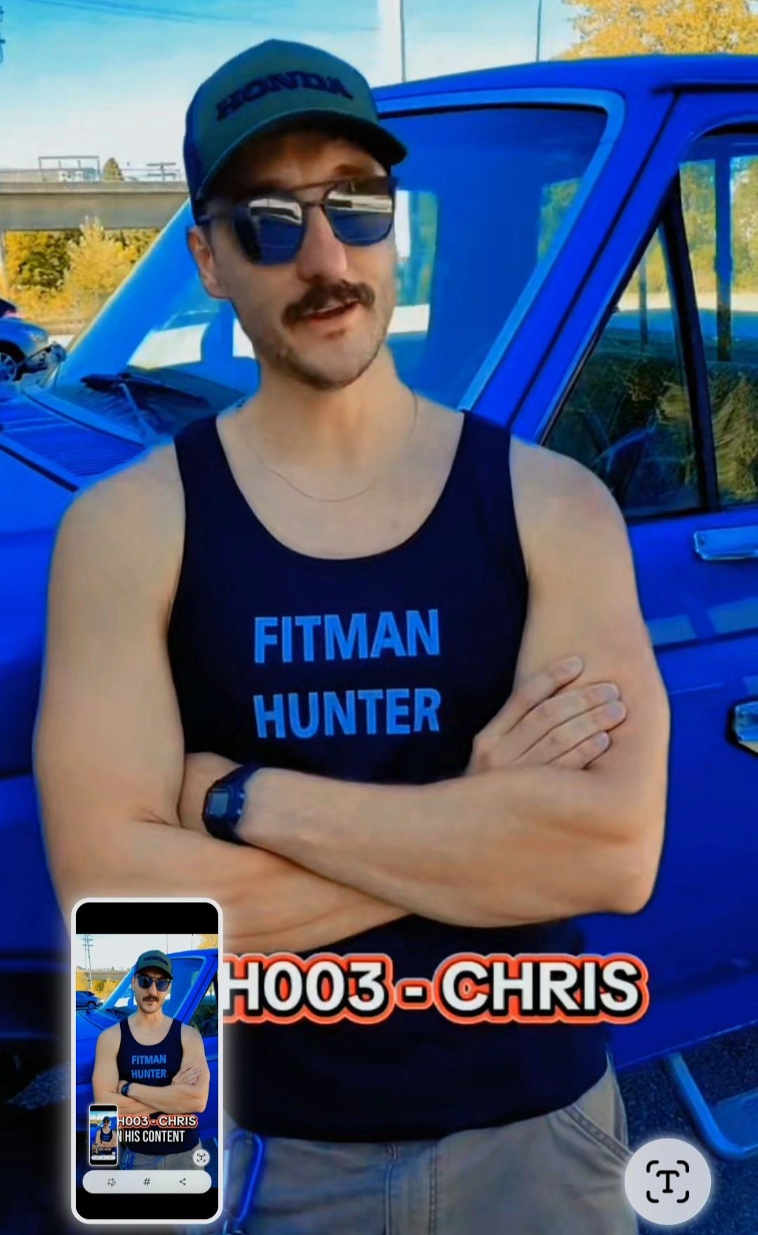 Man in a tank top and cap standing confidently by a blue vehicle.