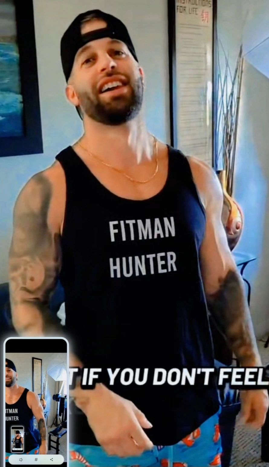 Muscular man in a "Fitman Hunter" tank top smiling indoors.