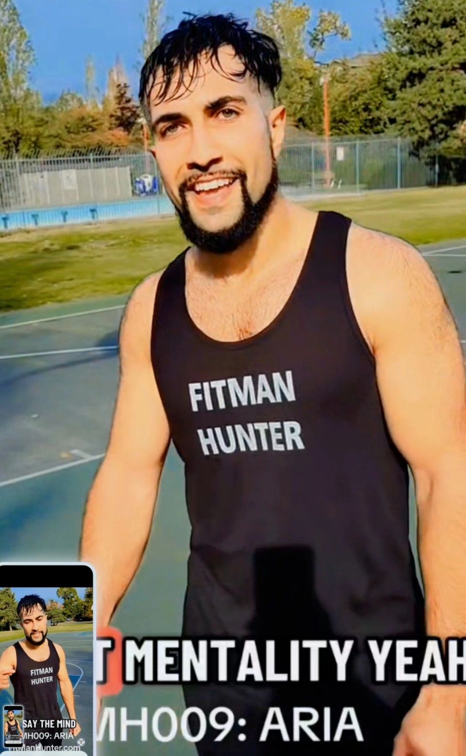 Smiling man in a black tank top with 'FITMAN HUNTER' text outdoors on a sunny day.
