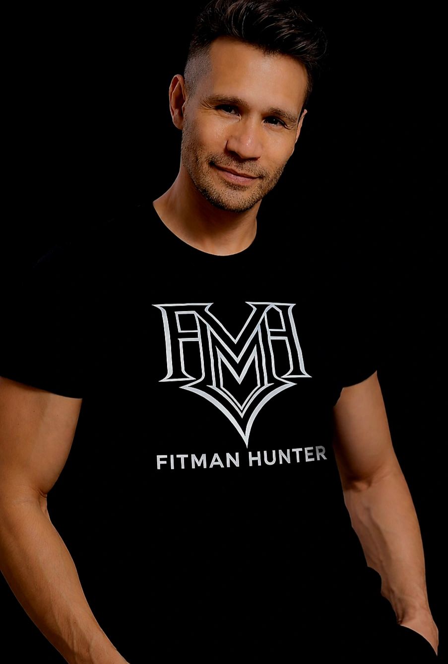 Man wearing a black Fitman Hunter t-shirt against a dark background.