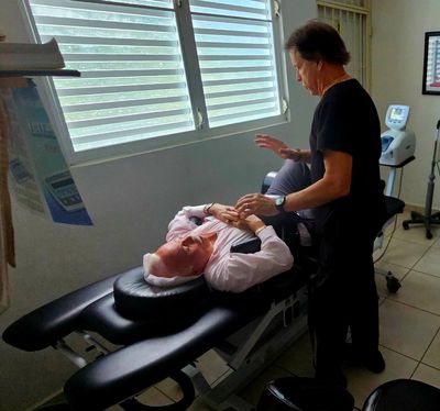 A man lying on a treatment table receiving care from a therapist in a clinical setting.