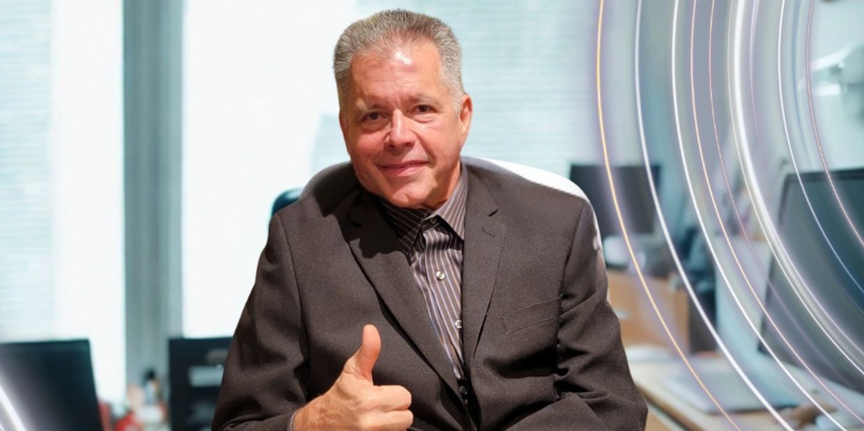 Smiling man in a suit giving a thumbs-up in an office setting.