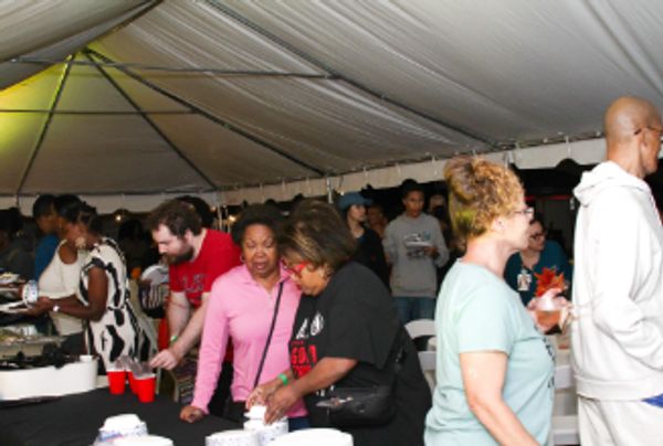 People gathered under a tent enjoying food and drinks at an event.