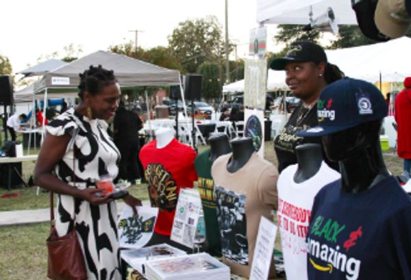 Two women at an outdoor market browsing a clothing stall with graphic t-shirts and hats.