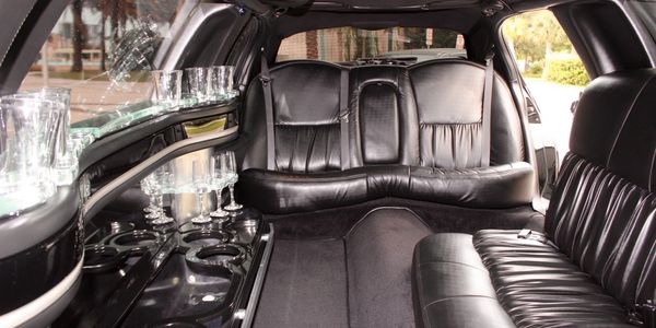 Luxurious black leather interior of a limousine with glassware and spacious seating.