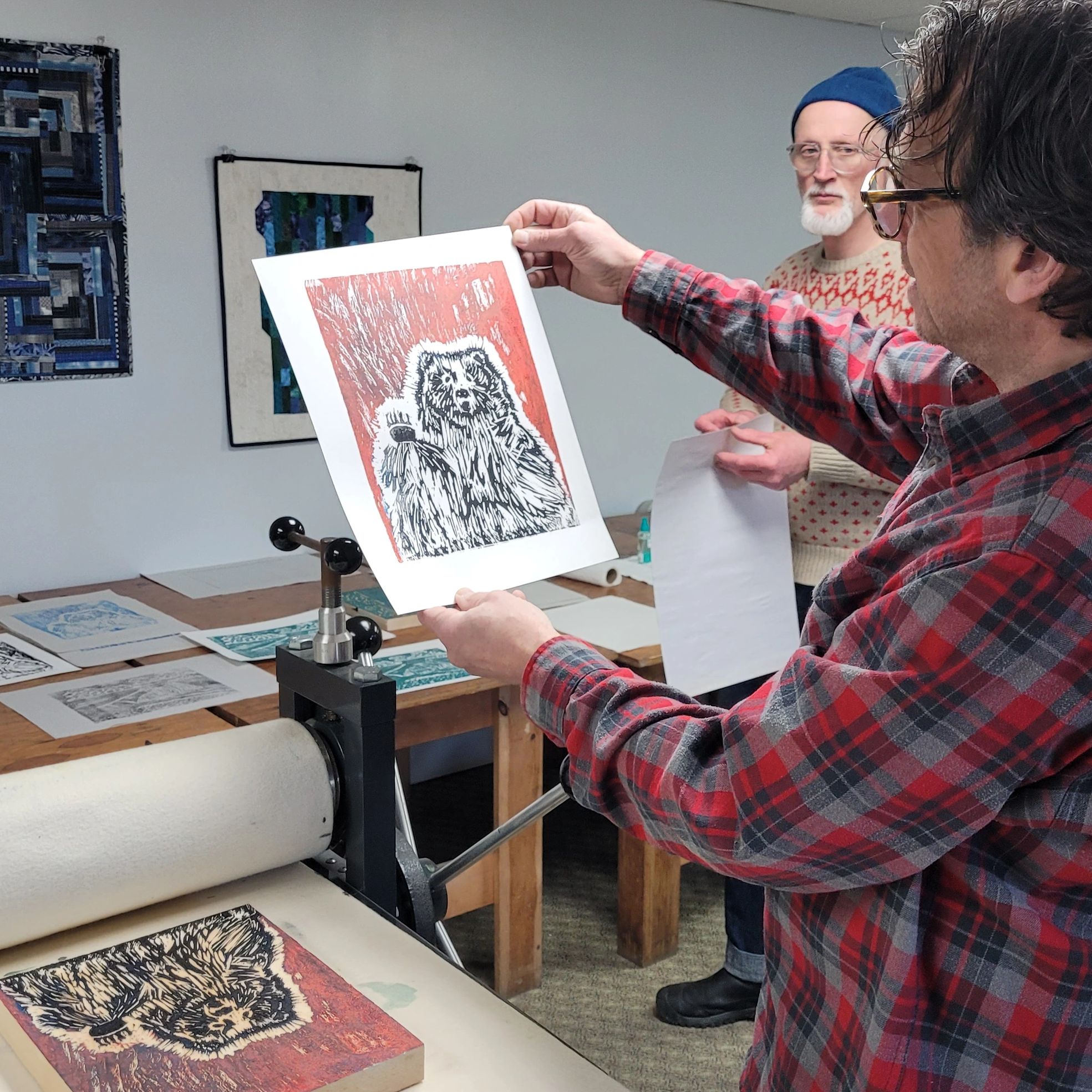 Two men examining a bear print made with a printing press after carving a wood block.