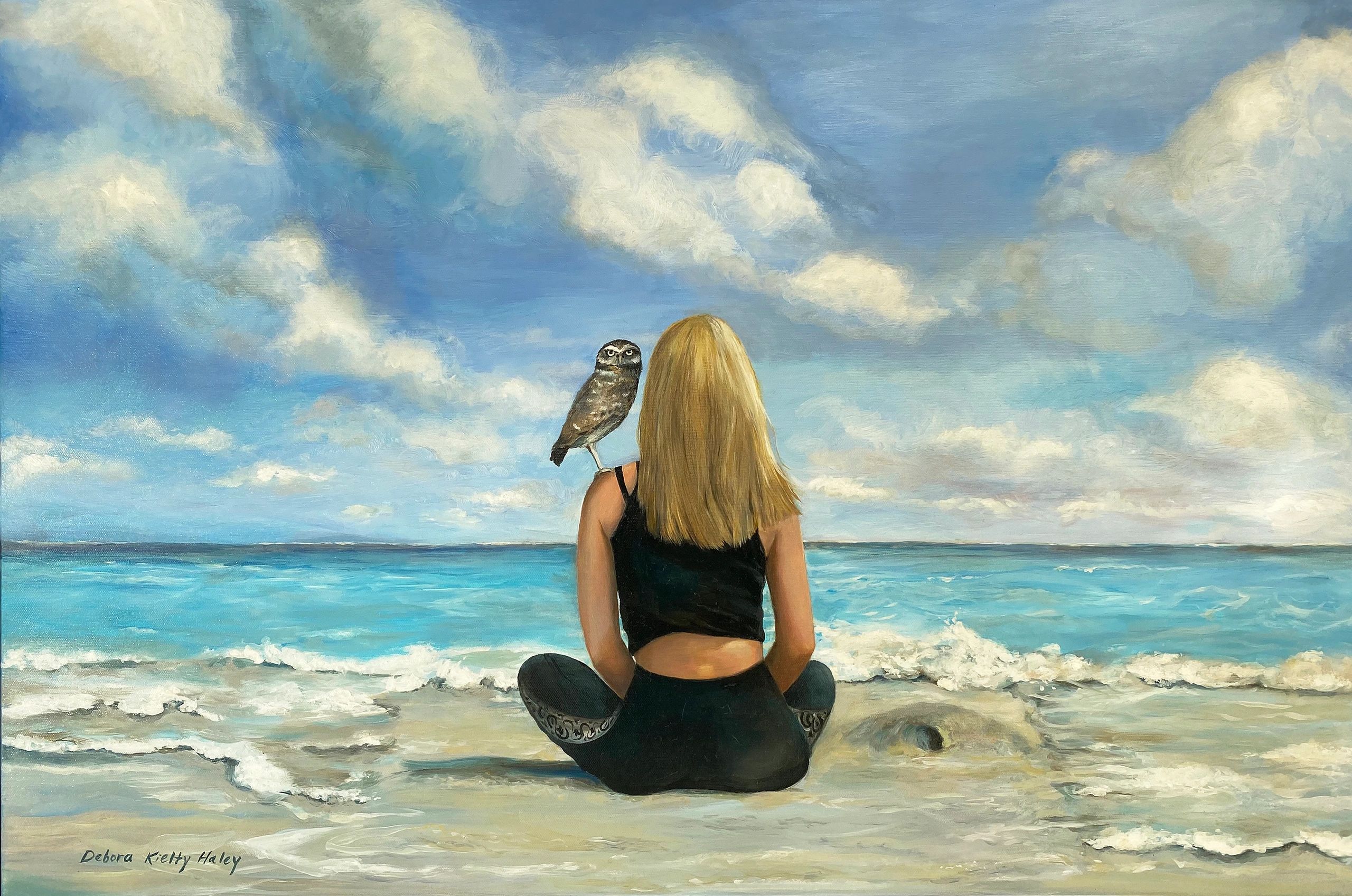 Woman sitting on beach with an owl perched on her shoulder under a cloudy sky.