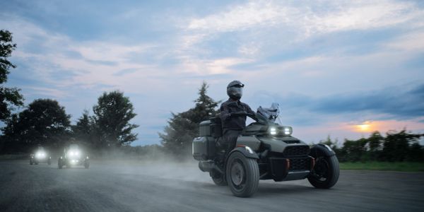 Riders on three-wheeled motorcycles at dusk.