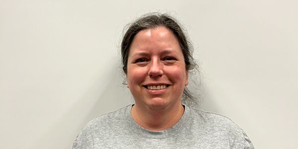 Smiling woman in a gray shirt against a plain wall.