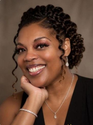 Smiling woman with braided hair, elegant jewelry, and a black outfit.