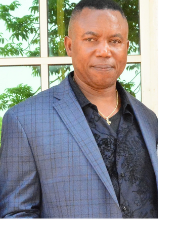 Man in a blue checkered blazer and black shirt posing outdoors.