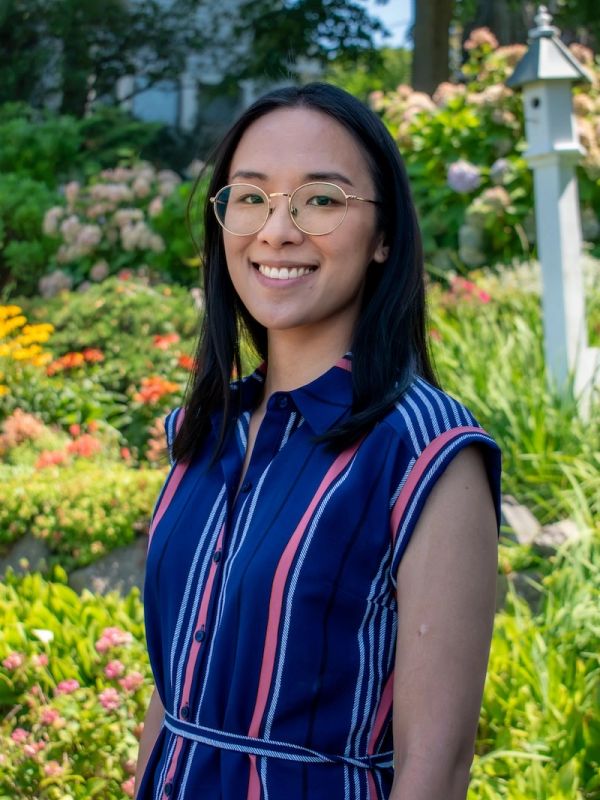A woman smiling in a garden wearing glasses and a striped dress.