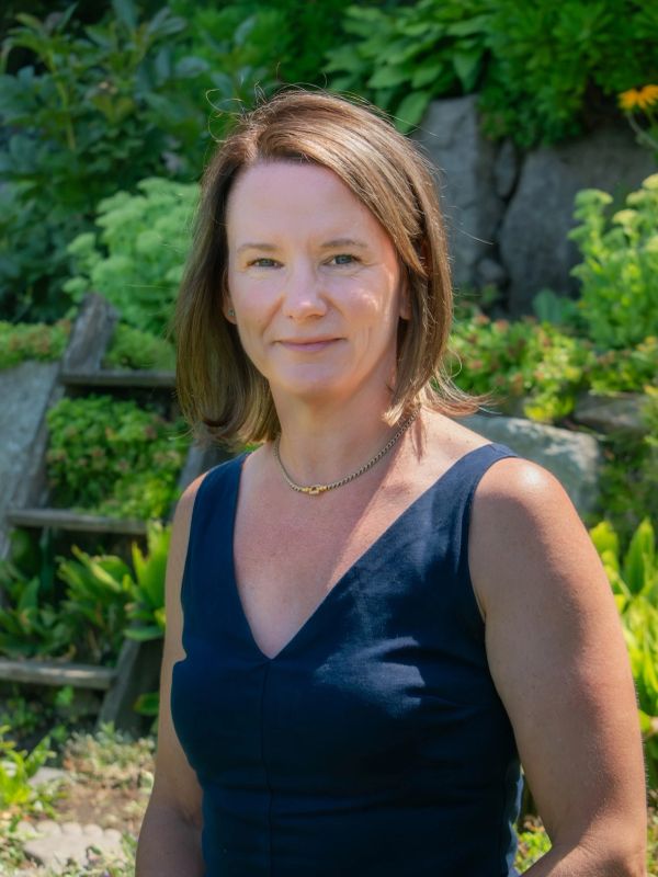 Woman standing outdoors in a garden wearing a navy dress.