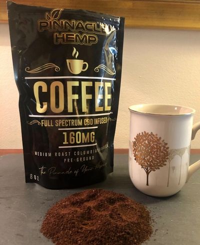 Bag of Pinnacle Hemp CBD infused coffee with ground coffee and a mug.