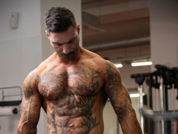 Muscular man with detailed tattoos in a gym setting.