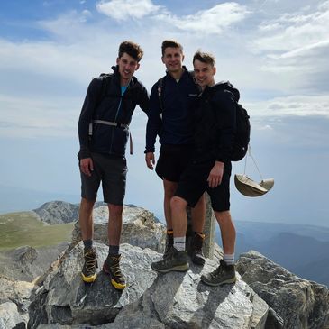 Three hikers posing on rocky mountain peak under a cloudy sky.